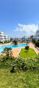 a large swimming pool with palm trees and buildings at Élégant appartement de 3 chambres vue piscine n4 in M'diq