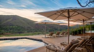 a pool with chairs and umbrellas on a deck at Botlierskop Tented Lodge in Reebok