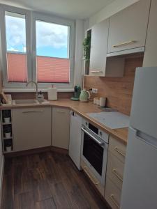 a kitchen with white cabinets and wooden floors and two windows at Apartament HARMONY in Koszalin
