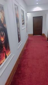 a hallway with a red carpet and paintings on the wall at Assala Hotel in Faisalabad