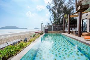 a swimming pool next to a beach next to a house at Cozy Beachfront Samroiyod in Baanphakrimlay 
