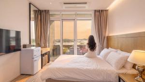 a woman sitting on a bed looking out the window at Goseong Moneblue Pension in Goseong