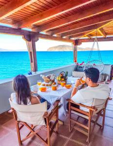 a man and woman sitting at a table on the beach at Tholos Alexandra's Beachfront House in Kavoúsion