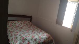 a bedroom with a bed with a floral bedspread and a window at Casa completa com piscina 12min da praia in Porto Seguro