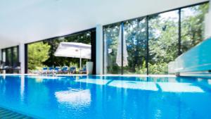 a large swimming pool with blue water and windows at Parkhotel Hohnstein by STEIGER Hotels in Hohnstein