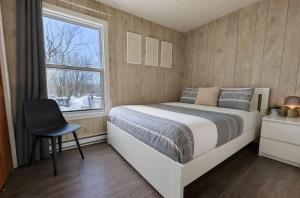 a bedroom with a bed and a window and a chair at Relaxing Chalet Getaway with Spa Fireplace & BBQ in Saint-Tite-des-Caps