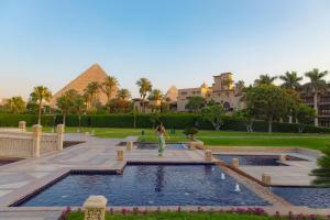 a woman standing in front of a swimming pool with a pyramid at Marriott Mena House, Cairo in Cairo