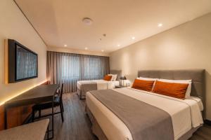 a hotel room with two beds and a desk at Laghetto Stilo São Paulo in São Paulo