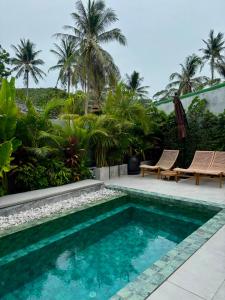 a swimming pool with two chairs and palm trees at Crown Chaloklum in Chaloklum
