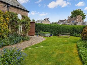 a garden with a bench and a clock on the side of a building at Ivy Cottage in Crieff