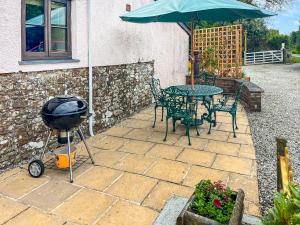 a grill and a table and chairs with an umbrella at Brook Cottage - Ukc9515 in Beaworthy