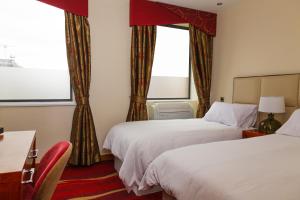 two beds in a hotel room with two windows at ICON Hotel in Luton