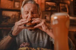 an older man eating a hamburger with his hands at The Wateredge Inn, Ambleside- The Inn Collection Group in Ambleside