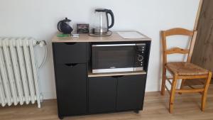 a microwave sitting on top of a black stand next to a chair at Chambre 8 in Le Trait