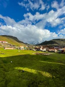 a green field with a town and mountains in the background at Hospedaje Vista Ausangate in Labramarca