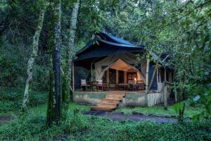 a tent with a table and chairs in the woods at Elephant Pepper Camp in Masai Mara