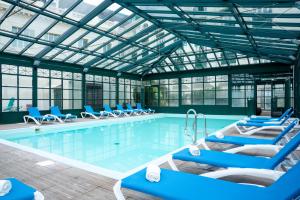 a swimming pool with blue lounge chairs in a building at SOWELL HOTELS Le Beach in Trouville-sur-Mer