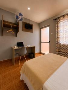 a bedroom with a bed and a desk with a laptop at Pensão Asa Branca in Assomada