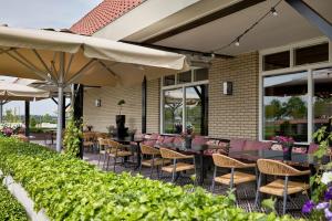 an outdoor patio with tables and chairs and umbrellas at Van der Valk Hotel Groningen Zuidbroek in Zuidbroek
