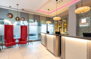 a hotel lobby with red chairs and a bar at Leonardo Hotel Munich City South in Munich