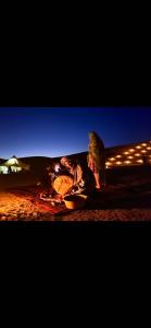 a person sitting next to a bonfire in the desert at night at Caravane du bonheur in Mhamid +1 photo