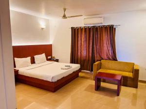 a bedroom with a bed and a chair and a window at Hotel Holiday Park,Thalassery in Green Island