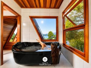 a woman laying in a tub in a room with windows at Chalés da Lagoa - Imaruí/SC in Imaruí