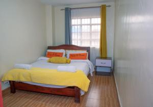a bedroom with a bed with a yellow blanket and a window at Micasa Homes BNB D2 in Limuru