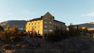 a large yellow building on a hill with mountains in the background at Esplendor by Wyndham El Calafate in El Calafate