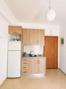 a kitchen with a white refrigerator and wooden cabinets at Velmare apartments in Paralia Vrachou