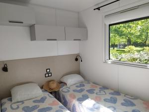 a small bedroom with two beds and a window at Camping LES ARBOUSIERS Carcans in Carcans