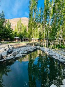 a pool of water with trees and a rock wall at Mystique Meadows Swiss Cottages in Nubra