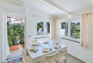 a dining room with a white table and chairs and windows at Villetta Mami in Ischia