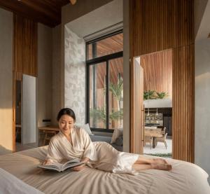 a woman laying on a bed reading a book at Award-Winning 3BR Villa 25m Pool Villa FEH in Kerobokan