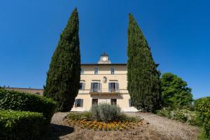 a building with a clock tower in the middle of two trees at Borgo Villa Certano - Case Vacanza in Toscana in Siena