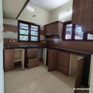 a large kitchen with wooden cabinets and windows at Trinity Mansion in Mangalore