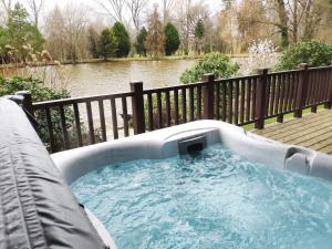 a hot tub on a deck next to a body of water at Kingfishers Woody Park in Willand