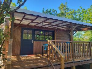 a cabin with a wooden deck with a blue door at Camping LES ARBOUSIERS Carcans in Carcans