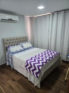 a bedroom with a bed with a purple and white comforter at Apartamento quarto e sala em campo grande in Cariacica