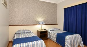 two beds in a room with blue curtains at Hotel Colonial Plaza in Itu