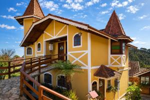 a yellow house with a brown roof at Pousada Palma Chalés in Monte Verde
