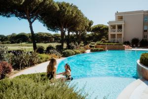 two women sitting next to a swimming pool at Kimpton Quinta da Marinha by IHG in Cascais