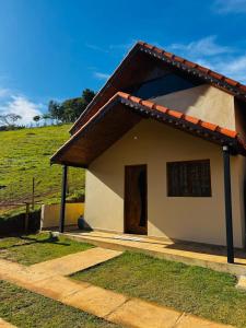 a small white house with a field in the background at Chalé Recanto Figueira in Camanducaia