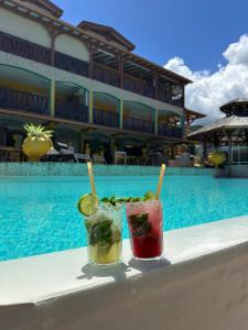 two cocktails sitting on a table next to a swimming pool at Résidence Simona Premium in Deshaies