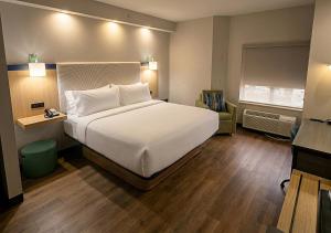 a bedroom with a large white bed and a chair at Garner Hotel Frederick Southeast by IHG in Frederick