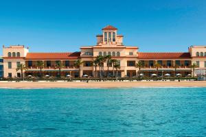 a large building with palm trees in front of the water at Le Meridien Ra Beach Hotel and Spa in El Vendrell