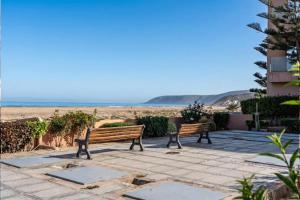 two benches sitting on a patio near the beach at Waterfront apartment in Imiouadar in Agadir nʼ Aït Sa