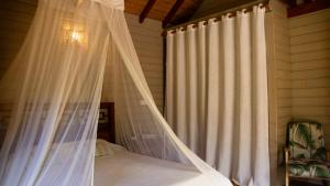 a canopy bed with a white curtain in a bedroom at Lodge Eden, SPA Privatif in Les Abymes