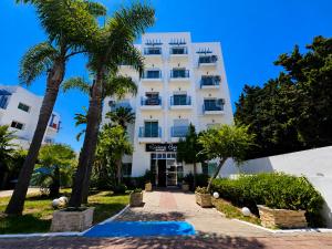a white building with palm trees in front of it at Cozy Studio Near Beach with Pool Access in Martil