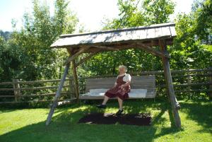 a little girl sitting on a bench under a canopy at Ferienwohnung Lahnerhof in Arriach